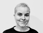 Schwarz-weiß-Porträt einer Person mit kurzem Haar, die direkt in die Kamera lächelt. Sie trägt einen dunklen Pullover.