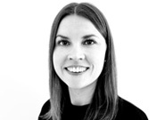 Frau mit glattem, schulterlangem Haar und dunklem Oberteil lächelt in die Kamera vor einem weißen Hintergrund. Schwarz-Weiß-Foto.