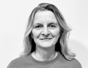 Porträt einer lächelnden Person mit halblangen Haaren vor einem weißen Hintergrund in Schwarz-Weiß.