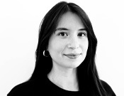 Schwarz-weiß-Porträt einer lächelnden Person mit langen, dunklen Haaren und Ohrring, vor einem einfachen Hintergrund.