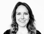 Porträt einer lächelnden Person mit langen Haaren, die nach vorne blickt. Das Bild ist in Schwarz-Weiß gehalten.