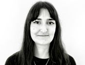 Schwarz-weiß Porträt einer lächelnden Person mit langen Haaren und Pony vor einem neutralen Hintergrund.