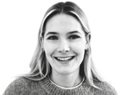 Porträt einer lächelnden Frau mit langen Haaren, die einen Pullover trägt. Sie blickt direkt in die Kamera vor weißem Hintergrund.