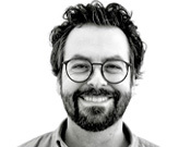 Porträt eines lächelnden Mannes mit Brille und Bart vor weißem Hintergrund.