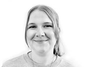 Porträt einer lächelnden Person mit langen Haaren, die ein helles Oberteil trägt, vor einem weißen Hintergrund.