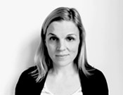 Schwarz-weiß Porträtfoto einer Person mit mittellangem Haar, die leicht in die Kamera lächelt. Sie trägt eine dunkle Jacke.