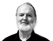 Porträt eines lächelnden Mannes mit Bart und schütterem Haar, blickt direkt in die Kamera vor einem weißen Hintergrund.