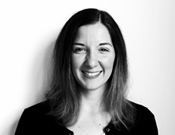 Porträtfoto einer lächelnden Frau mit schulterlangem Haar vor einem weißen Hintergrund, in Schwarz-Weiß gehalten.