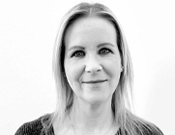 Frau mit glattem, schulterlangem Haar lächelt dezent in die Kamera, vor einem weißen Hintergrund. Schwarzweiß-Foto.