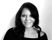 Schwarz-weiß Porträt einer lächelnden Frau mit mittellangem dunklem Haar vor weißem Hintergrund.