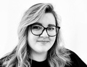 Eine Person mit Brille und welligem Haar lächelt leicht in die Kamera. Das Bild ist in Schwarz-Weiß gehalten.