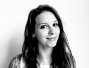 Eine Person mit langen Haaren lächelt leicht in die Kamera, vor einem neutralen Hintergrund. schwarz-weiße Fotografie.