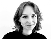 Schwarz-weiß-Porträt einer lächelnden Person mit schulterlangem Haar und hellem Hintergrund.